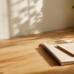 Minimal morning workspace with a notebook and water glass in natural sunlight.