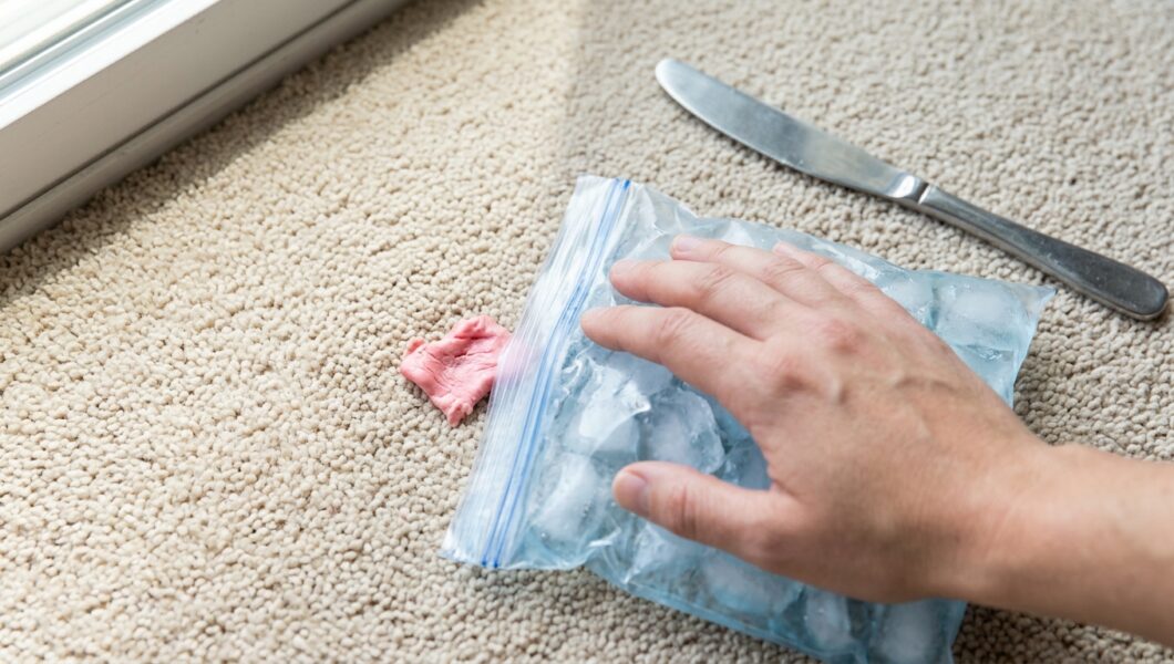 Hand using a dull knife to lift frozen chewing gum from beige carpet
