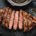 Sliced pan-seared wagyu steak with heavy marbling and a medium-rare center on a dark plate