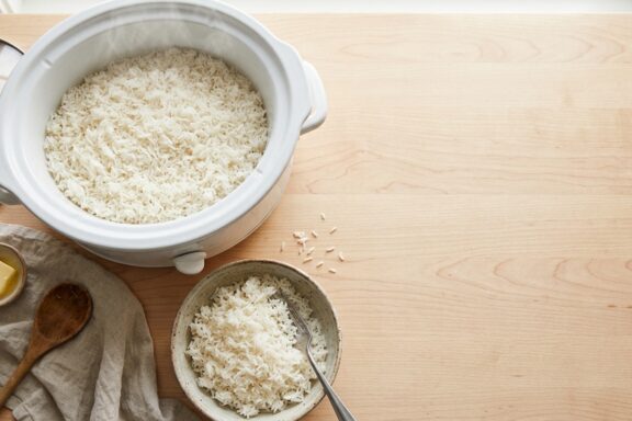 Bowl of fluffy white rice next to an open slow cooker on a kitchen counter