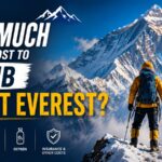 An eye-catching infographic YouTube thumbnail titled "HOW MUCH DOES IT COST TO CLIMB MOUNT EVEREST?". On the right side, a mountaineer in a yellow and black down suit with a blue backpack stands on a snowy ridge, looking toward a massive, snow-covered mountain peak. On the lower left side, four white icons outline the major expenses: PERMITS, EXPEDITION PACKAGE, OXYGEN, and INSURANCE & OTHER COSTS. The background features a dramatic view of rugged mountain ranges under a clear blue sky.